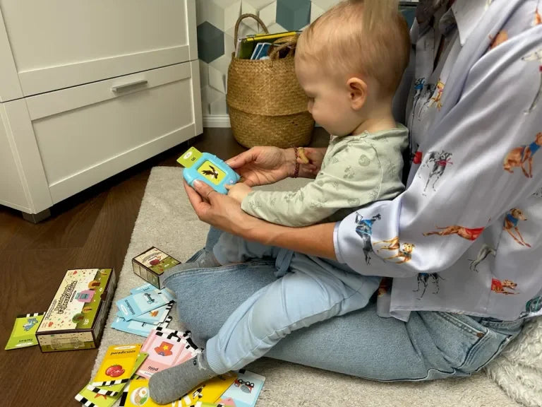 Majka i beba zajedno koriste KinderSpeech edukativni čitač kartica dok sjede na podu, okruženi setom slikovnih kartica za rani razvoj govora i jezika.